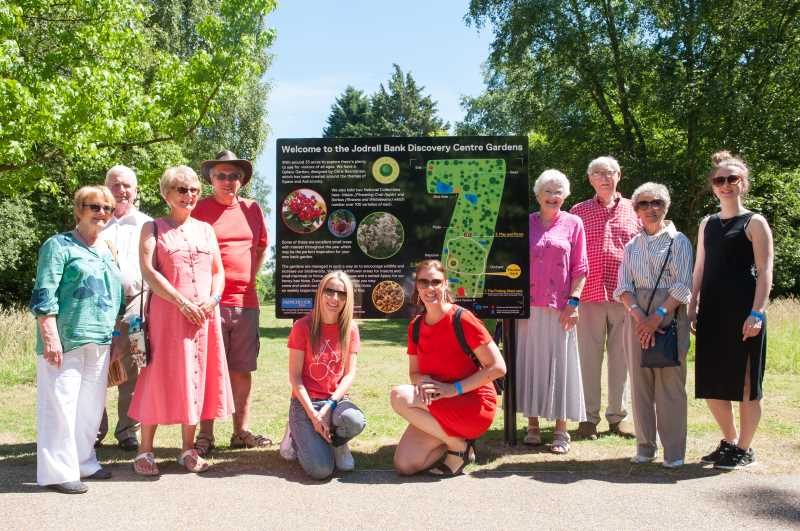 Mixed group of smiling members in front of a sign at Jodrell Bank on their day out.