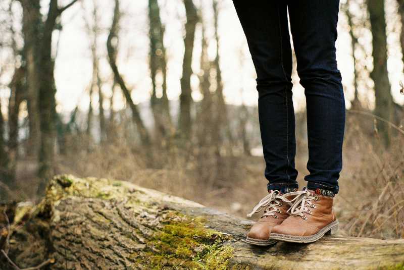 Woman's feet in walking boots stood on a log in a forest in autumn.