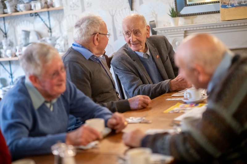 Four older men sta having a coffee together in a cafe.