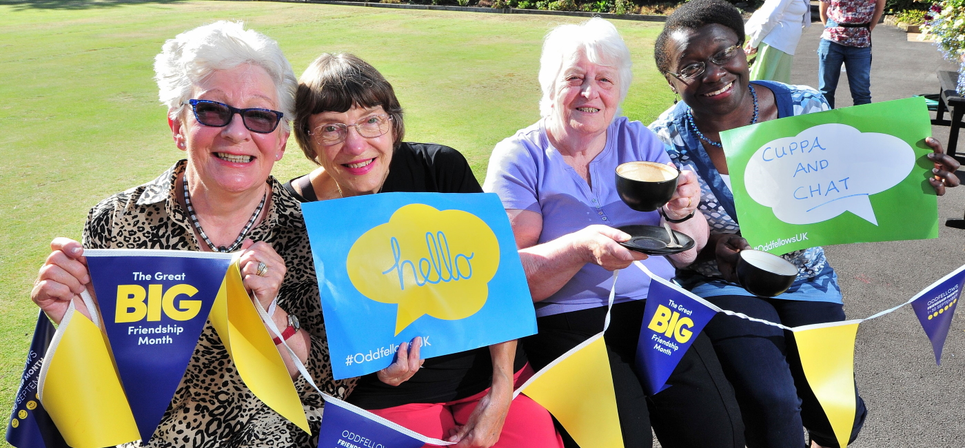 Four members holding up Friendship Month buntings and welcoming signs