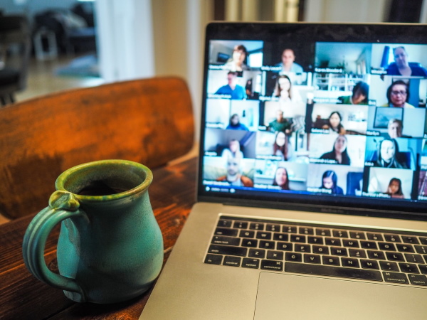 Amug next to a laptop showing peoples faces on a video conferencing app