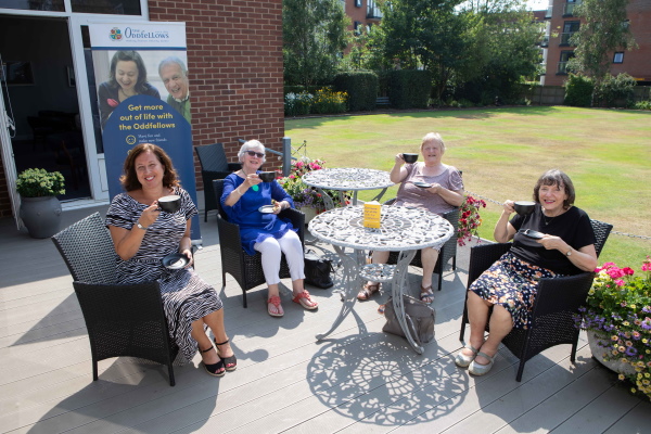 A group sitting in a garden drinking coffee and smiling at the camera