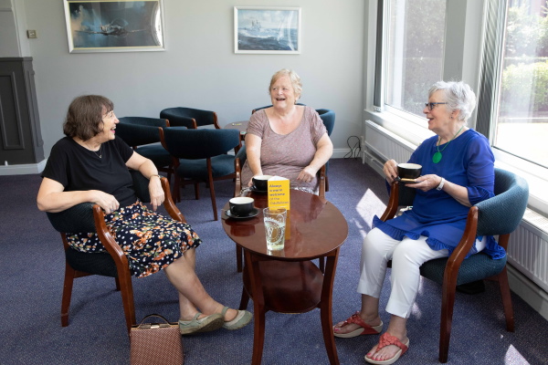 Three women sat around a coffee table talking and drinking from mugs