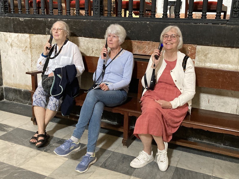 Three women sat on a bench in a museum