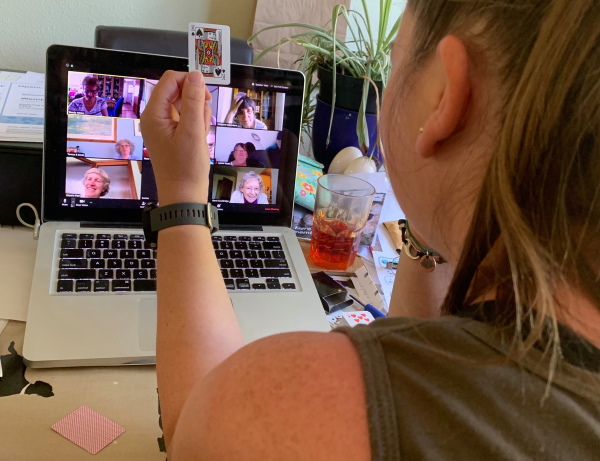 A lady sitting in front of a laptop playing cards with friends, via video conferencing app, Zoom.