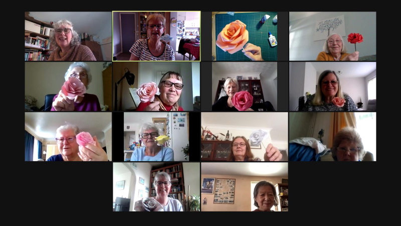 Zoom screen of members holding up paper flowers made in a craft session.