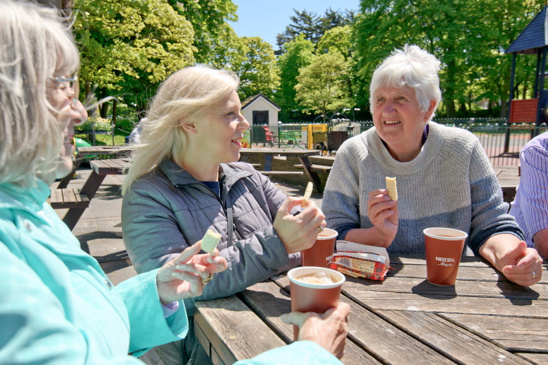 Three ladies at a park cafe having a cup of tea and a biscuit together