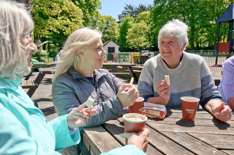 Julie and fellow member enjoying a coffee in the sunshine at a park bench.