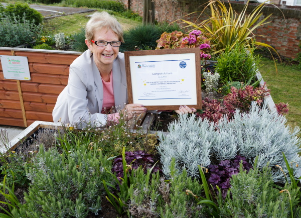 Wendy smiling at the camera and holding her Making a Difference certificate for 'working in the spirit of mutuality'
