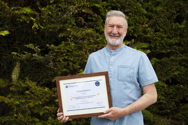 Paul holding his Making a Difference Award certificate and smiling in his garden