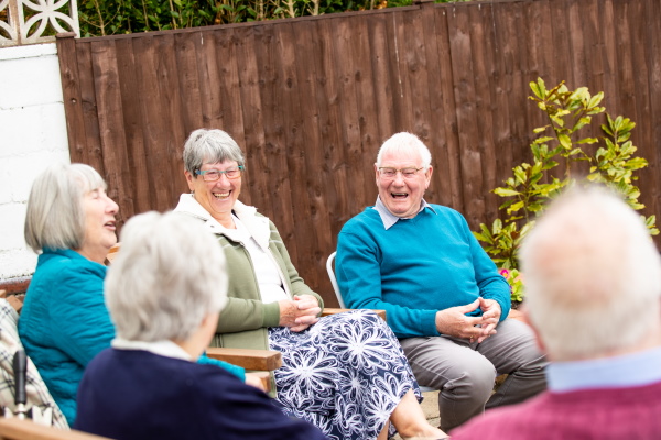 A group of men and women sitting outside, chatting and laughing