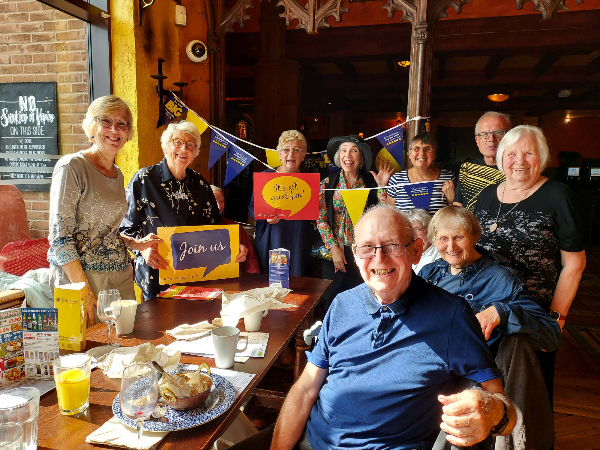 Members coming together at a lunch holding friendship month signs and bunting