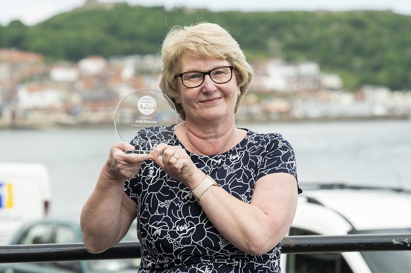 Julie with her award in front of a backdrop of Scarborough