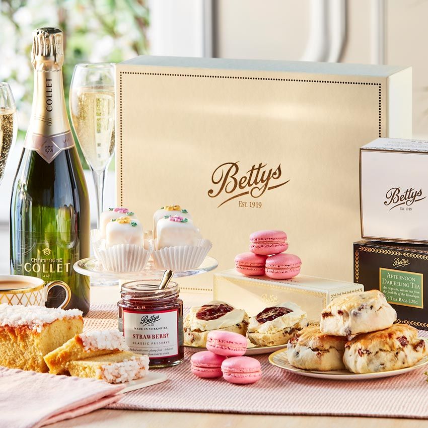 A box with Bettys written on it and its contents of various sweet treats jam and a bottle of champagne