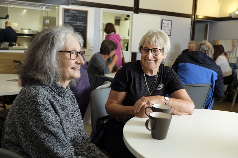 Two women in their 60s in a cafe having a cup of tea together