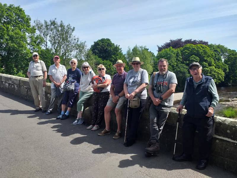9 members perched on a bridge in the countryside taking a break on a group walk
