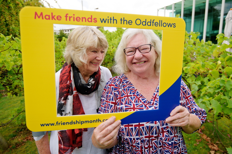 Two ladies looking through a colourful frame that says Make friends with the Oddfellows