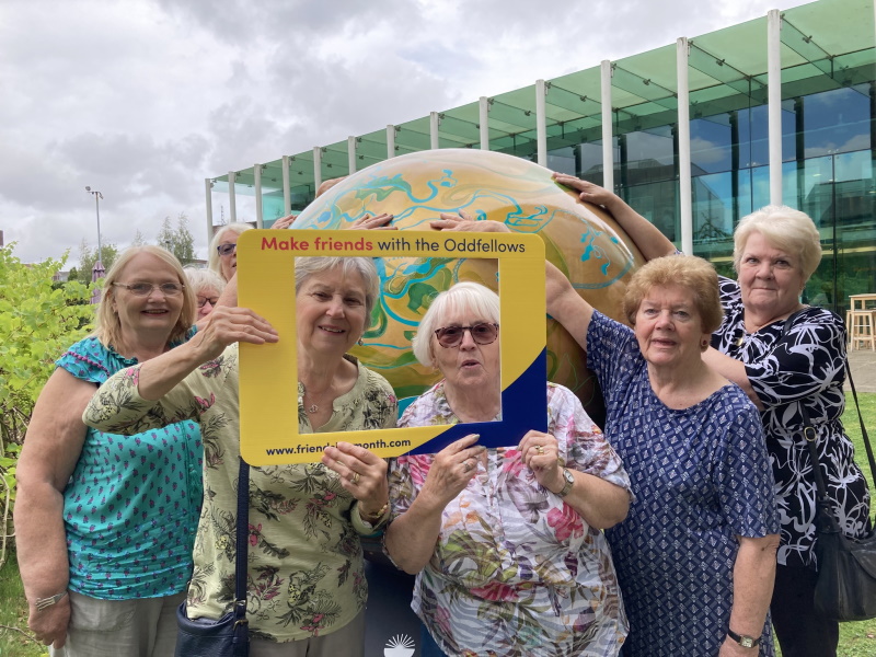 A group of ladies gathered around a glass globe, posing for a picture and holding up a frame