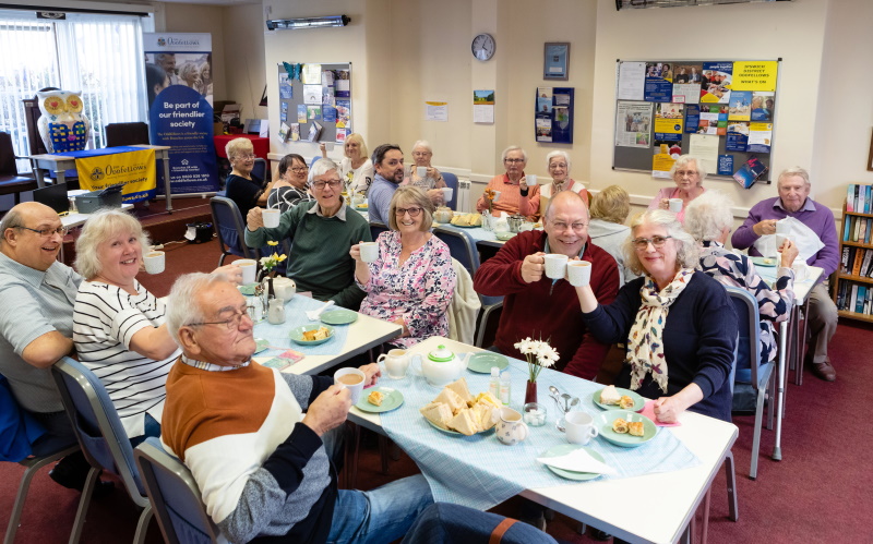 People sitting at tables enjoying a cream tea, turning to smile at the camera