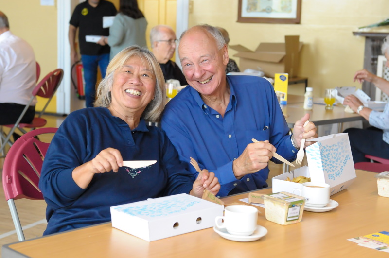 A man and a women are sitting at a table smiling at the camera as they tuck in to a portion of fish and chips