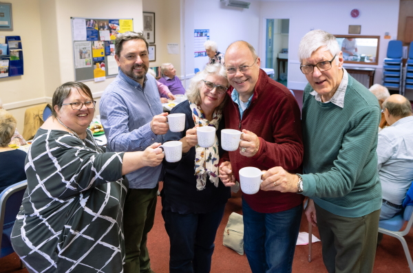 Group of five friends, including Teresa and Kevin, chinking mugs of tea together and smiling.