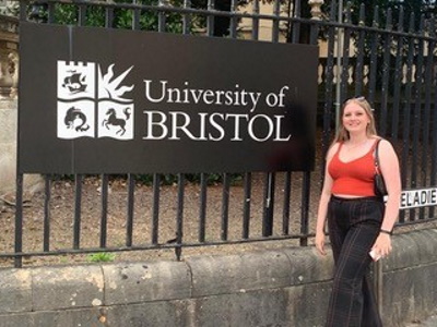 Francesca brennan Brown stood by a sign for the University of Bristol