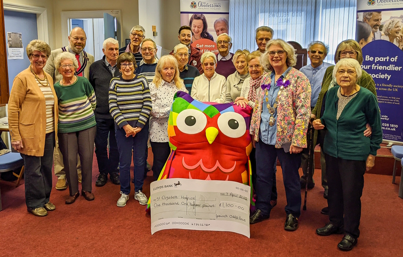 Members grouped together around a massive colourfully-painted owl statue and a big cheque.
