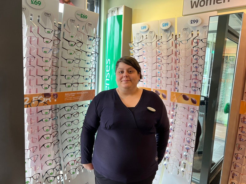 Kerry Luckett smiles at the camera stood in front of racks of glasses