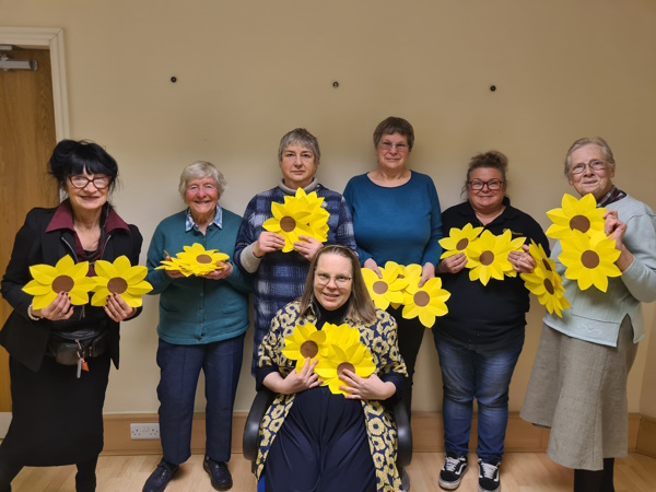 The group of women smile at the camera while holding the paper sunflowers they crafted