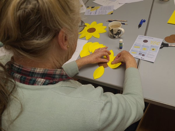 An woman sticks the yellow paper petals around a brown paper centre to create a sunflower