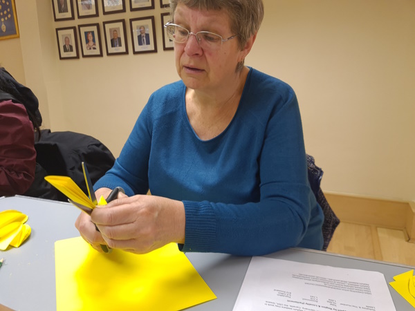 A woman is seated while cutting yellow paper to create the petals for the sunflowers