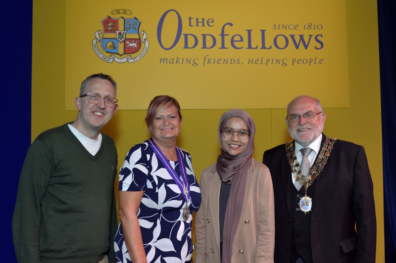 Professor Edd James, Jane Nelson, Nur Zainal, and David Ogden smile at the camera with the Oddfellows sign in the background