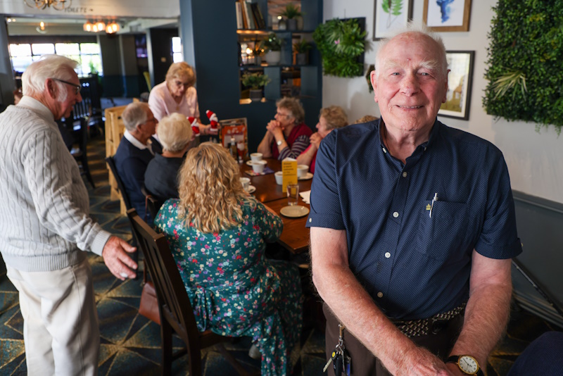A man in the foreground with people sat around a table in the background