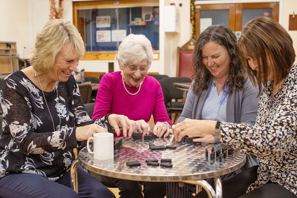 Four women smile and laugh while playing dominos
