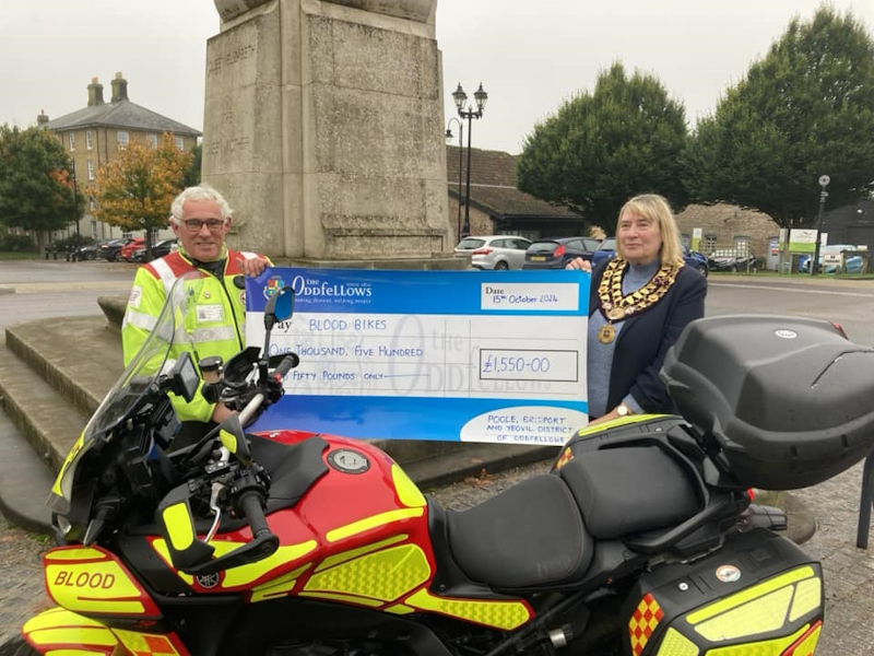 Two representatives holding a big cheque next to a blood bike.