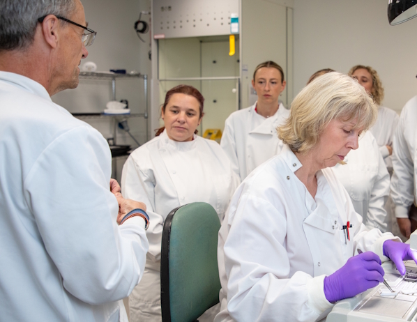 Representatives from the Oddfellows on a lab tour. All are wearing white lab coats and listening to a talk from someone at the Manchester Cancer Research Centre