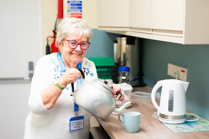 A woman pouring a cup of tea from a big teapot