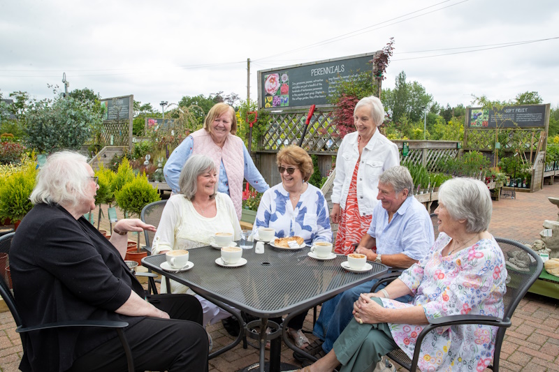 A group of people sat around a table outside drinking coffee