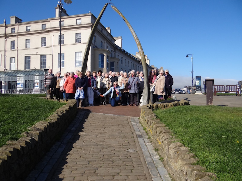 A large group of people pose for a photograph on a sunny day in Whitby