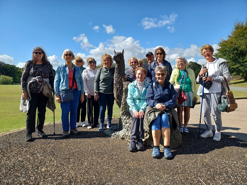 A group of people on walk posing around a statue of an alpaca