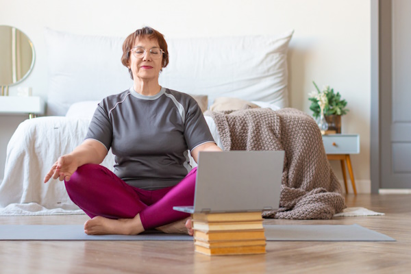 A woman sitting cross legged on the floor, meditating with a laptop in front of her