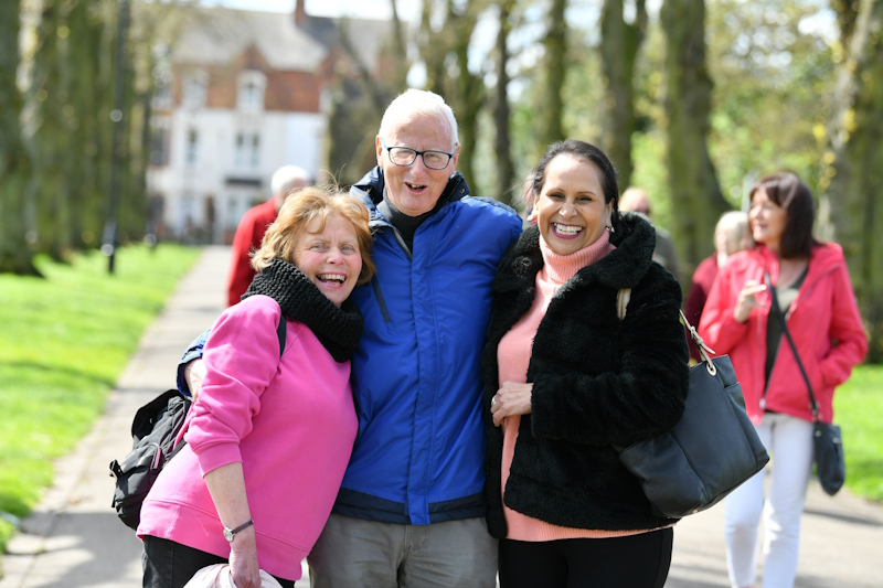 Three Oddfellows members stood in a group smiling. They are off on a walk in a park