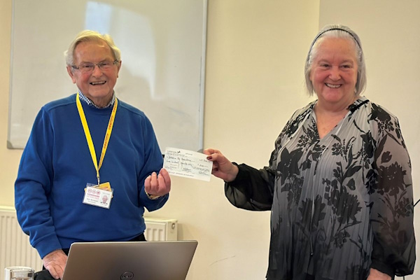 A man and a woman smile at the camera while holding a cheque