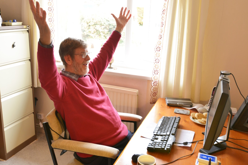 A man sat at a computer with his hands in the air