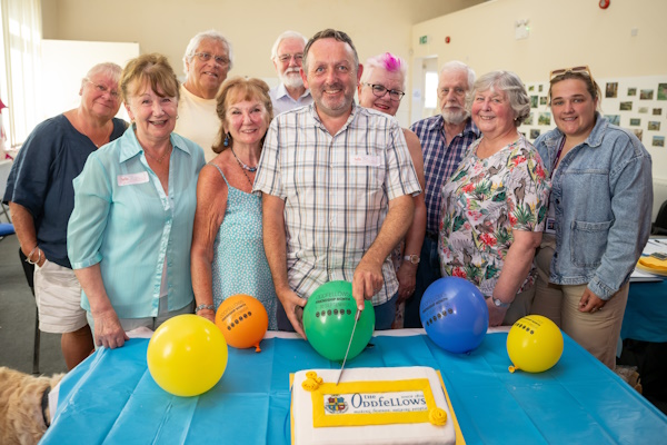 A group of people pose with an Oddfellows cake and balloons