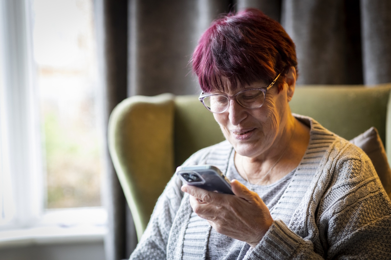 oman sat in a chair smiling at something on her mobile phone