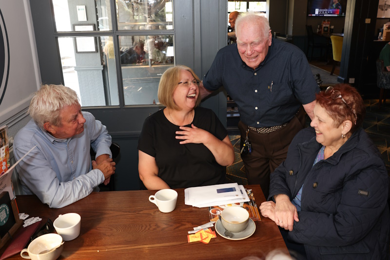 Four people around a table laughing and drinking coffee