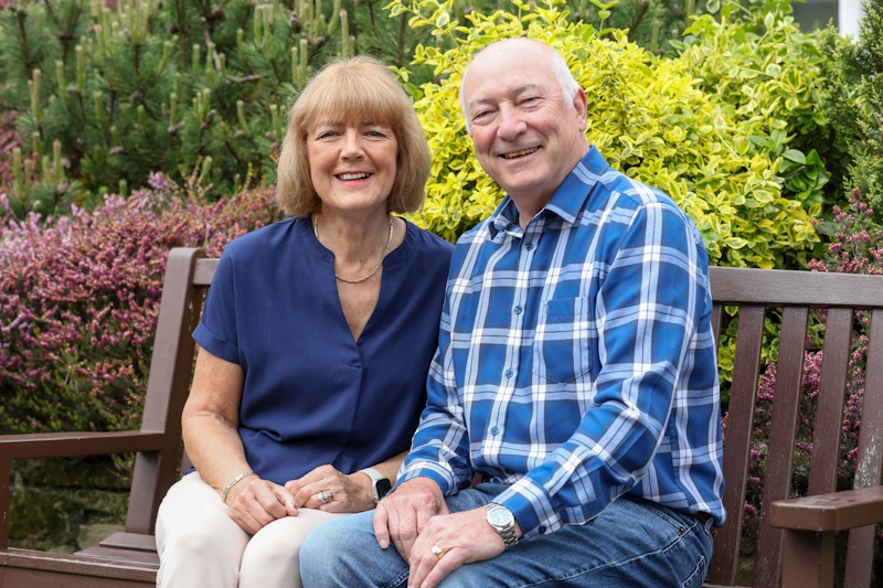 Joan and Jimmy O Shaughnessy sat together on a bench in a park. They are both smiling