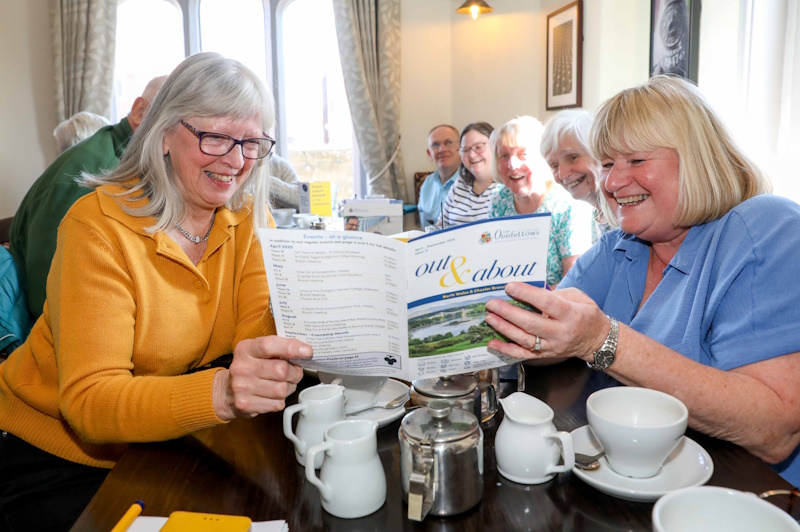 two women reading a magazine together with a coffee morning happening in the background