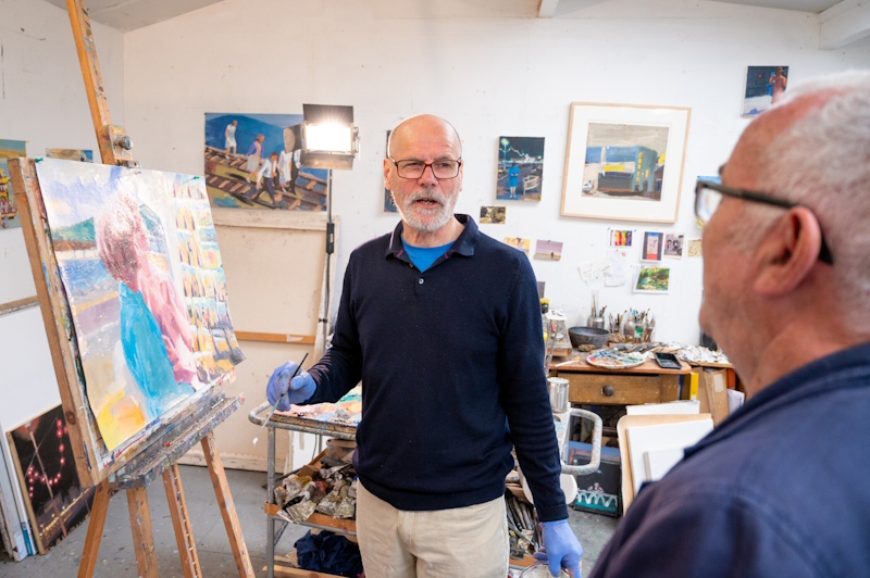 Two men in an artist's studio. One man is painting on a canvas